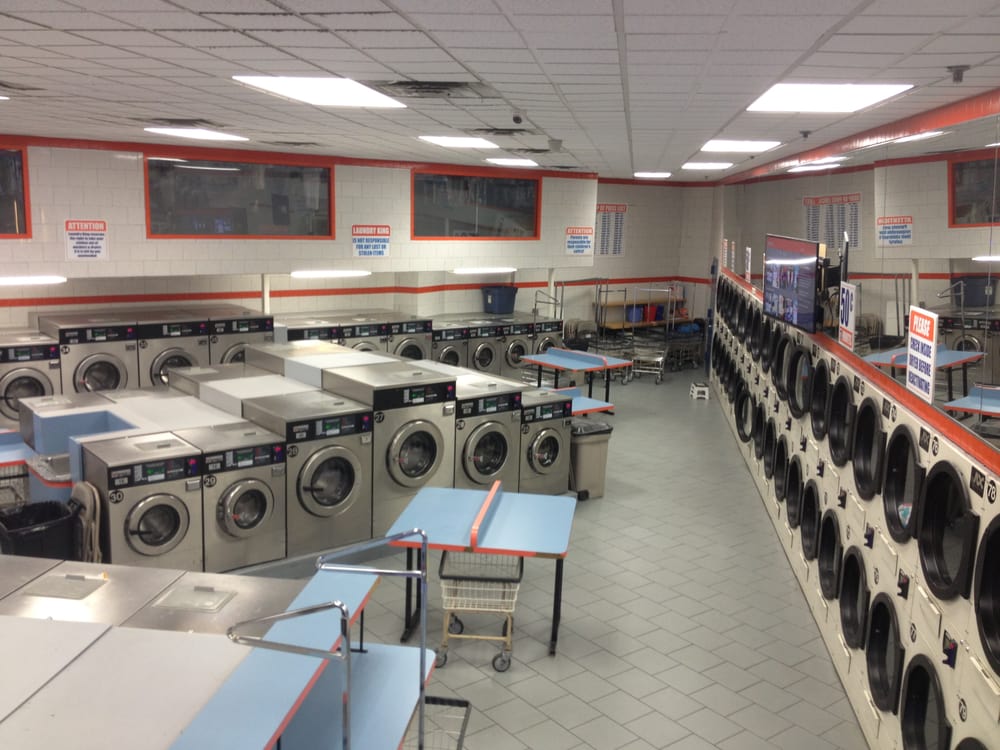 Rows of washers and stacked dryers with folding tables at the Laundry King self-service laundromat on Neptune Avenue in Brooklyn
